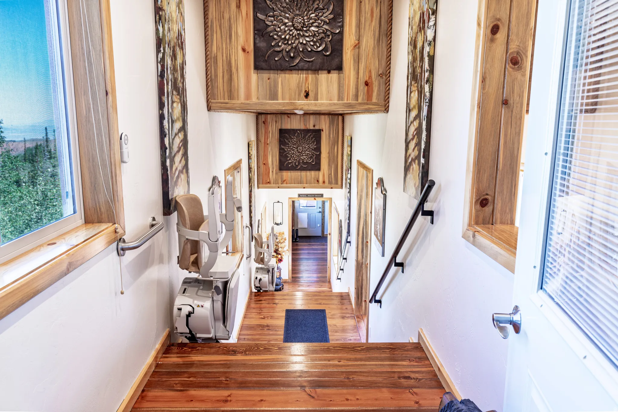 Hardwood steps and flooring, natural wood window trim, white painted walls, and a black metal handrail