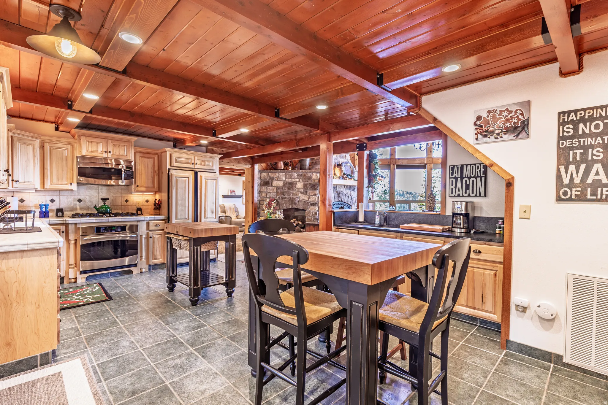 Wood-beamed ceiling, tile flooring, wood-finish cabinetry, built-in stainless steel appliances, and a butcher block island