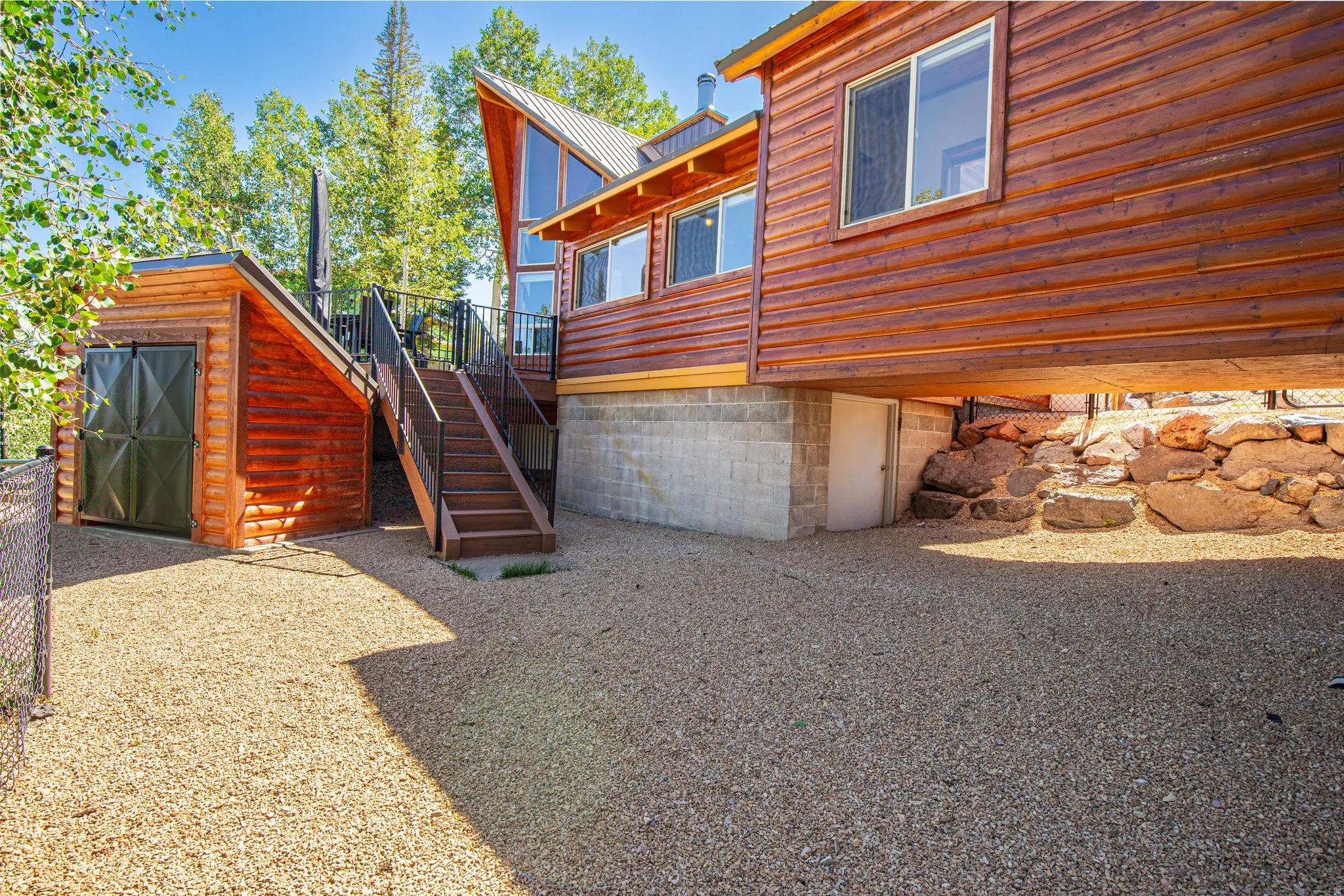 Wood-sided exterior with expansive windows, a gravel ground surface, and a multi-level deck featuring metal railings