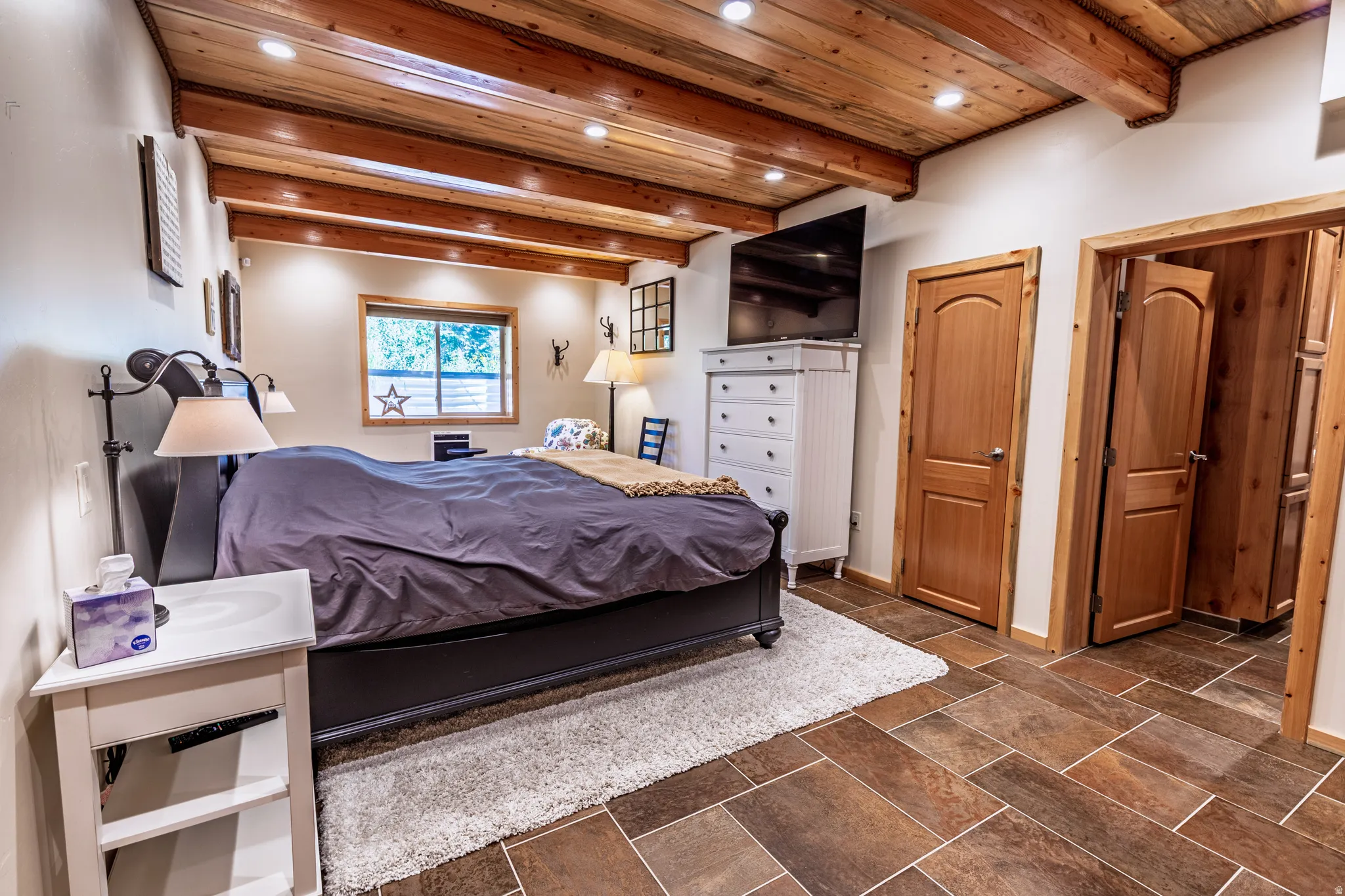 Exposed wood beam ceiling with recessed lighting, tile flooring, wood-finish doors, and a window with natural light