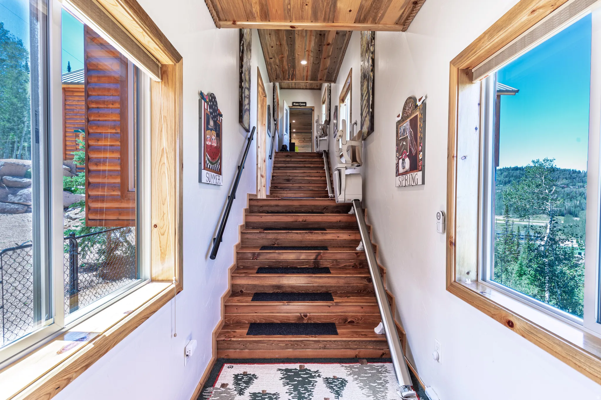 Wood-finish stairs with dark handrails, surrounded by white walls and wood-trimmed windows