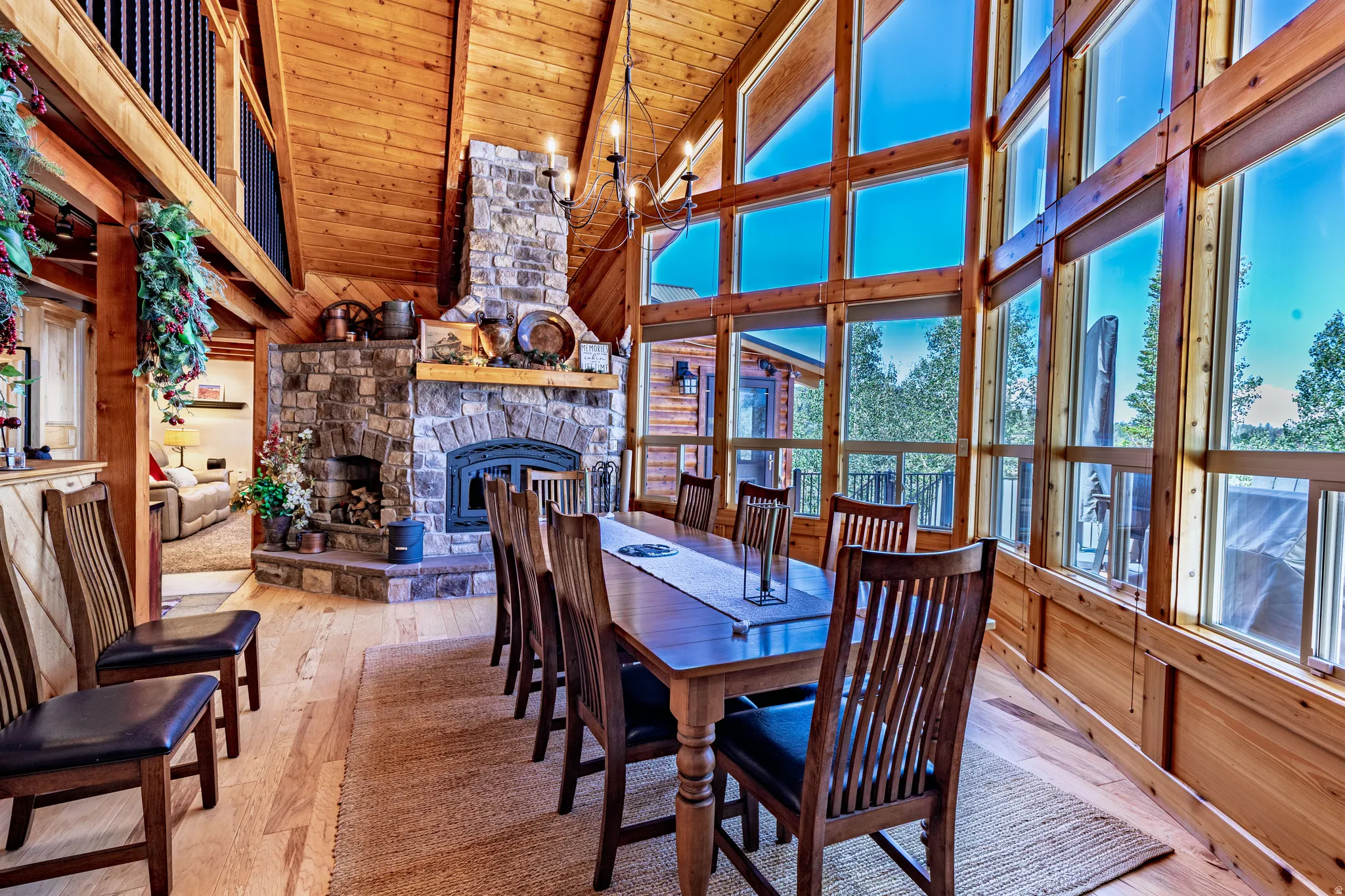 Vaulted wood-paneled ceiling, floor-to-ceiling windows, stone-clad fireplace, wood-finish flooring, and a built-in balcony