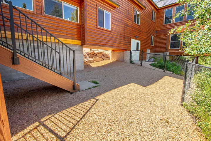 Wood-paneled exterior featuring multiple windows, gravel ground cover, and a black metal fence