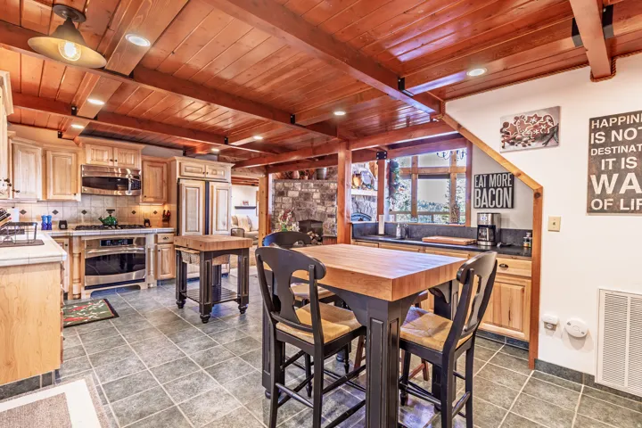 Wood-beamed ceiling, tile flooring, wood-finish cabinetry, built-in stainless steel appliances, and a butcher block island