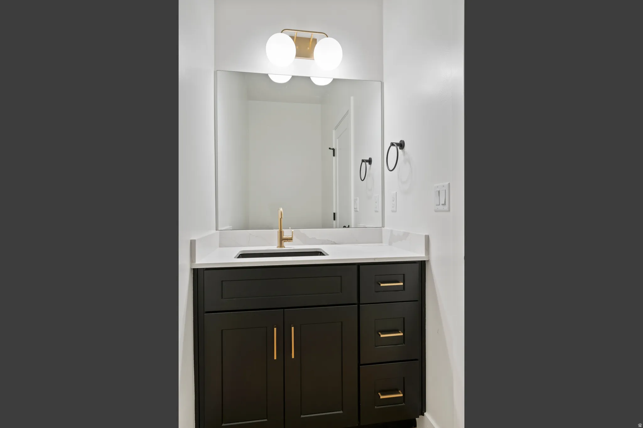 Dark wood-finish vanity with gold-tone hardware, white countertop, rectangular undermount sink, and a gold-tone faucet