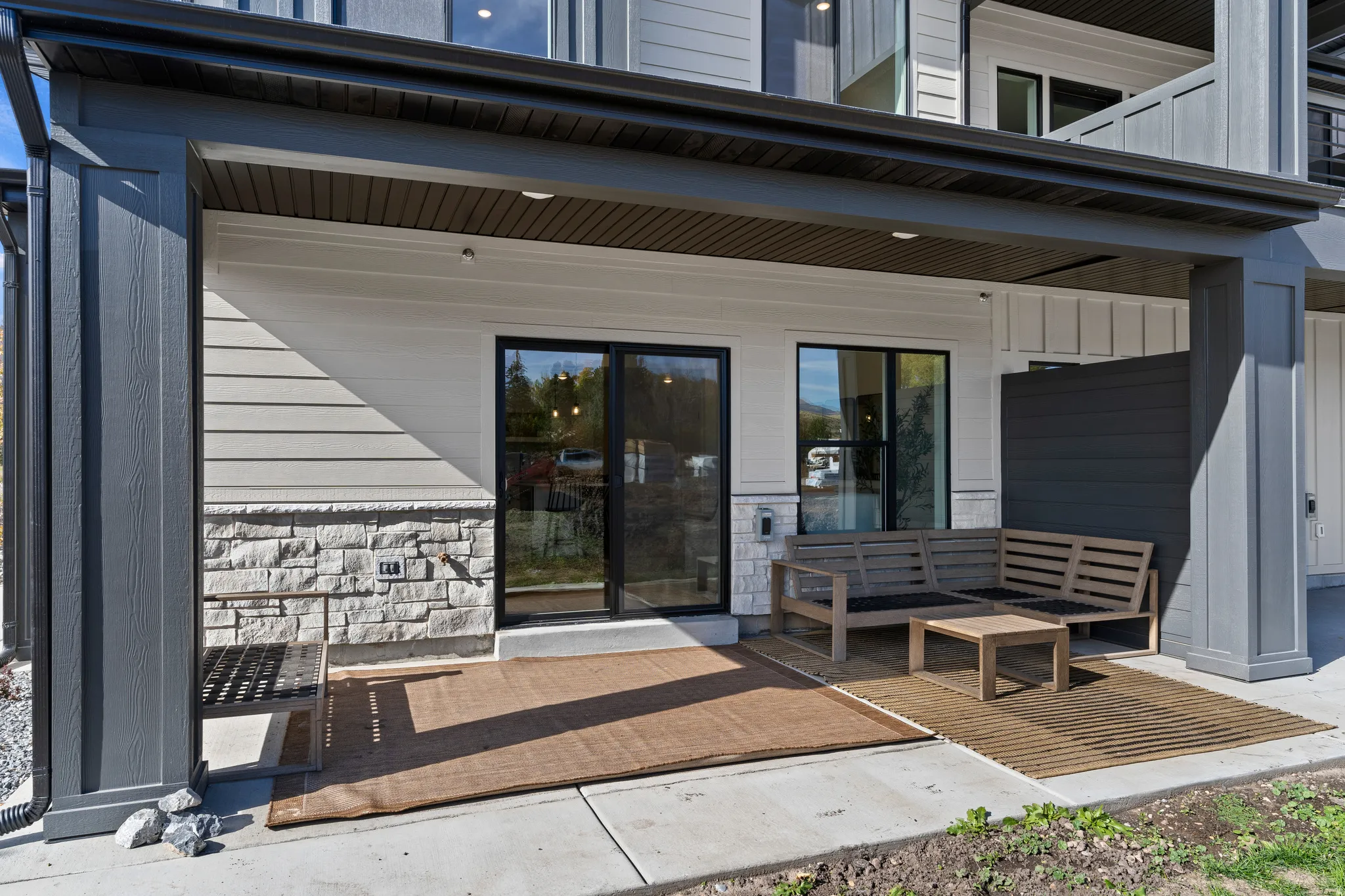 Covered patio featuring a sliding glass door, stone veneer detailing, and exterior siding