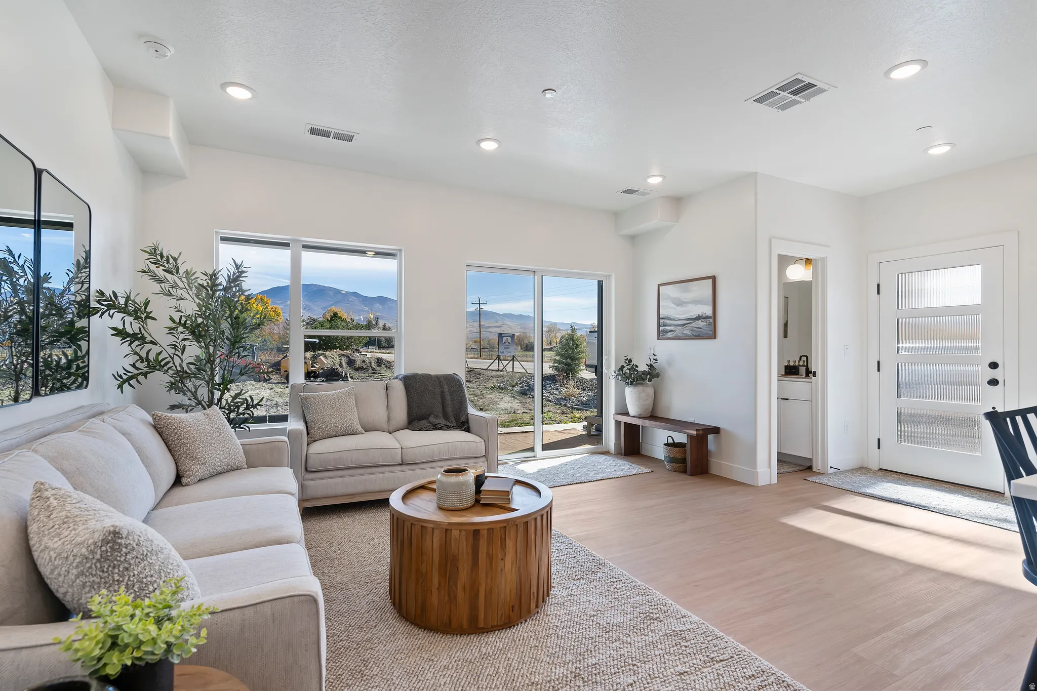 Recessed lighting illuminating the open living area, featuring wood-finish flooring and large windows
