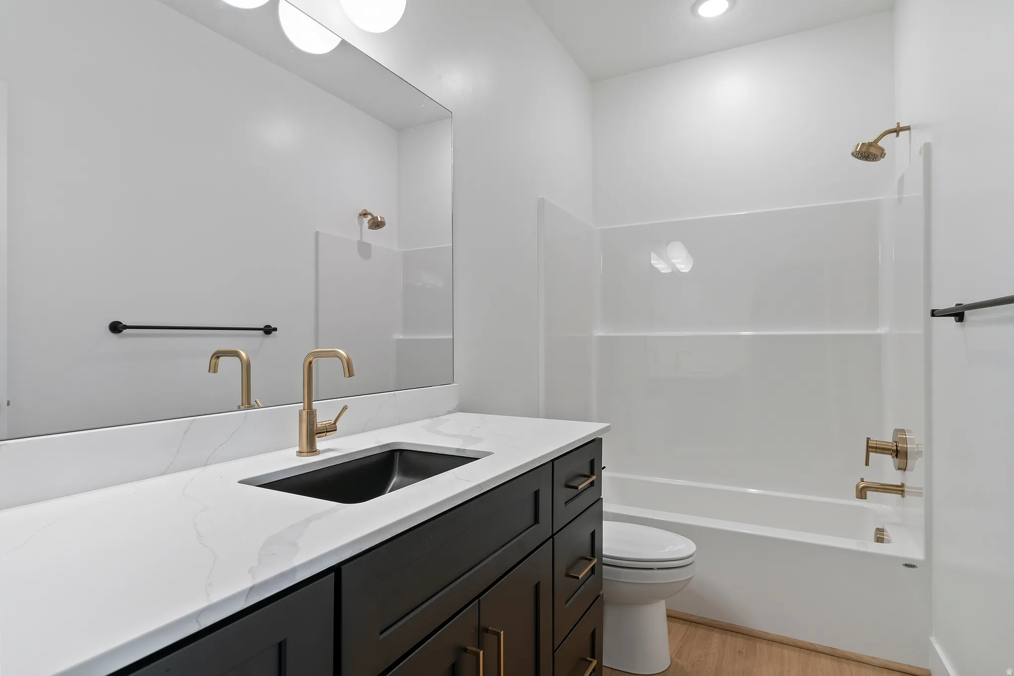 White quartz countertop with an undermount sink, dark wood-finish vanity with brass hardware, polished brass faucet, and a large wall-mounted mirror
