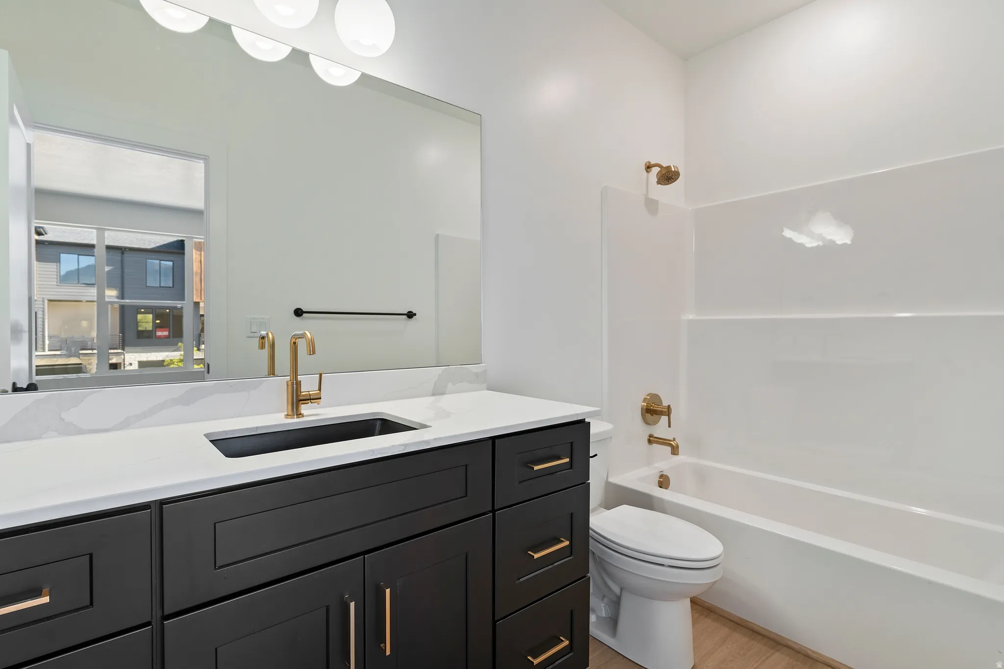 Vanity with a black cabinet, white countertop, and gold-finish fixtures