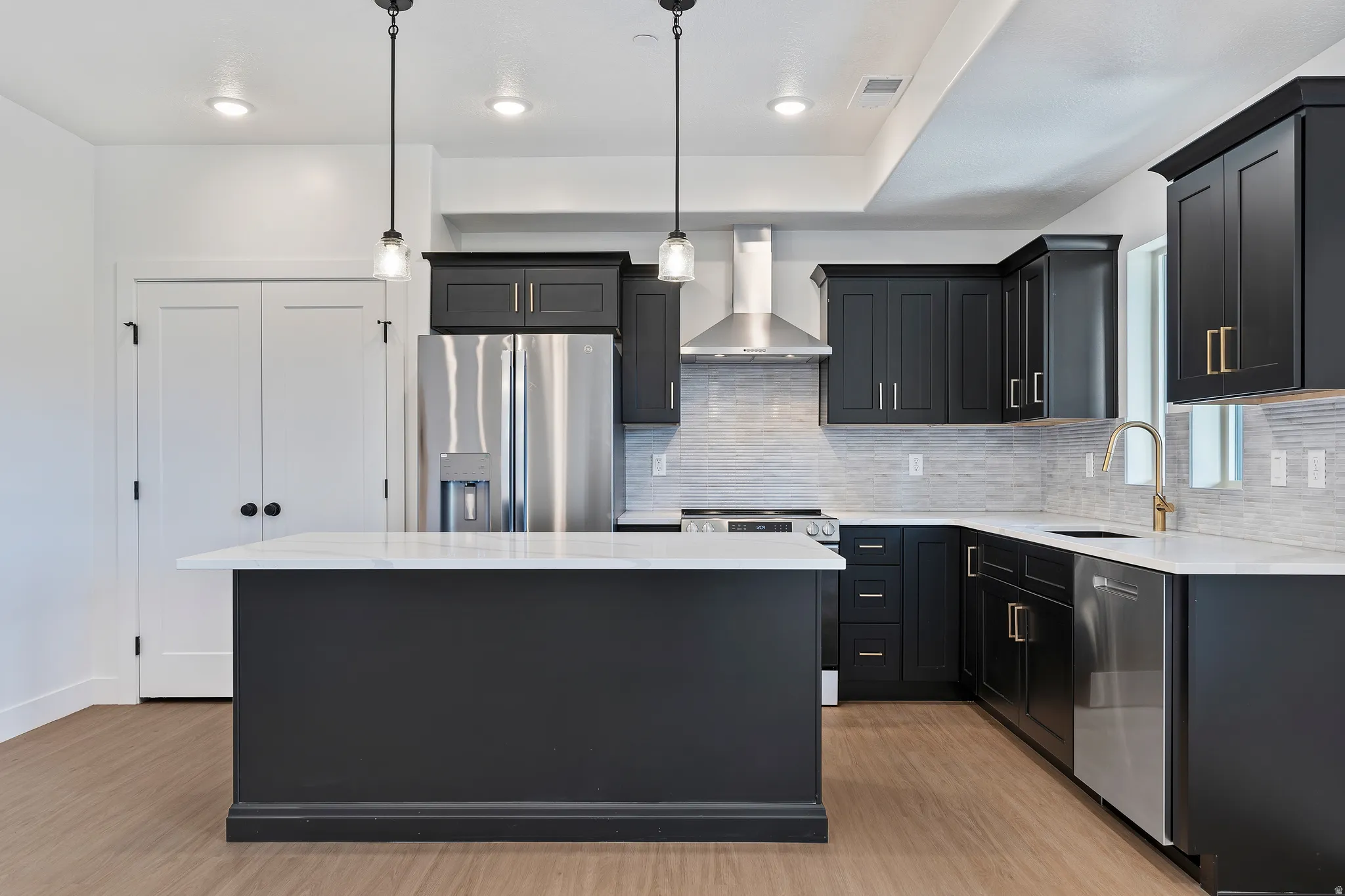 Gourmet kitchen with dark cabinetry, stainless steel appliances, a white island countertop, wood-finish flooring, and pendant lighting