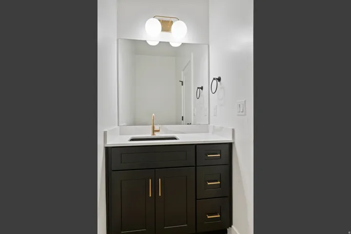 Dark wood-finish vanity with gold-tone hardware, white countertop, rectangular undermount sink, and a gold-tone faucet