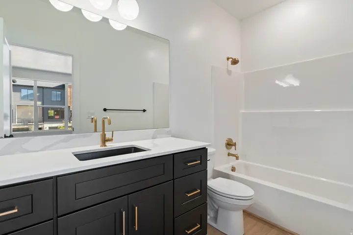 Vanity with a black cabinet, white countertop, and gold-finish fixtures