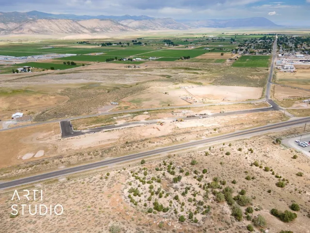 Expansive land featuring paved road access, adjacent agricultural fields, and distant mountain ranges