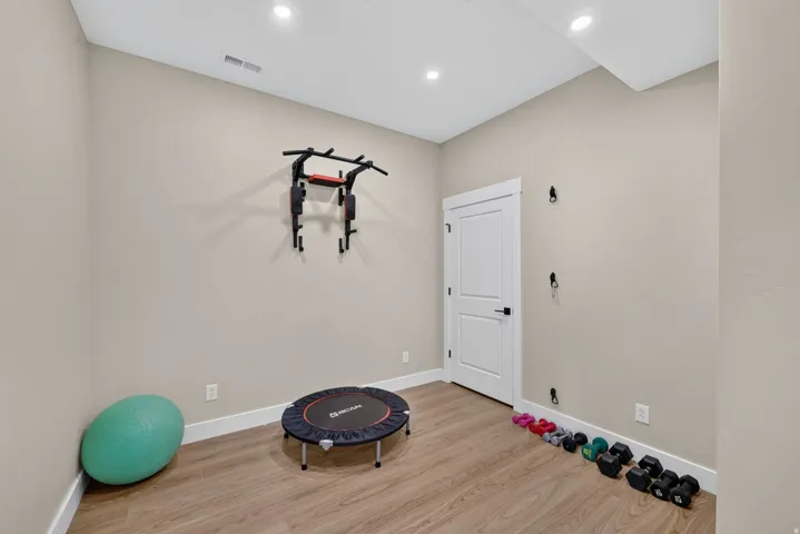 Recessed lighting, light-toned walls, wood-finish flooring, white trim, and a white interior door with black hardware