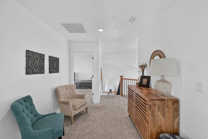 Carpeted hallway with white walls, wood-finish railing, and recessed lighting