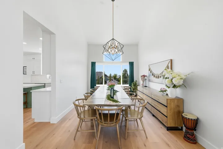 Vaulted ceiling with geometric chandelier, light wood-finish flooring, white walls, and a large window with ample natural light