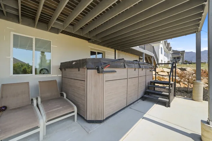 Covered concrete patio featuring a hot tub with steps, and a rock-lined garden bed