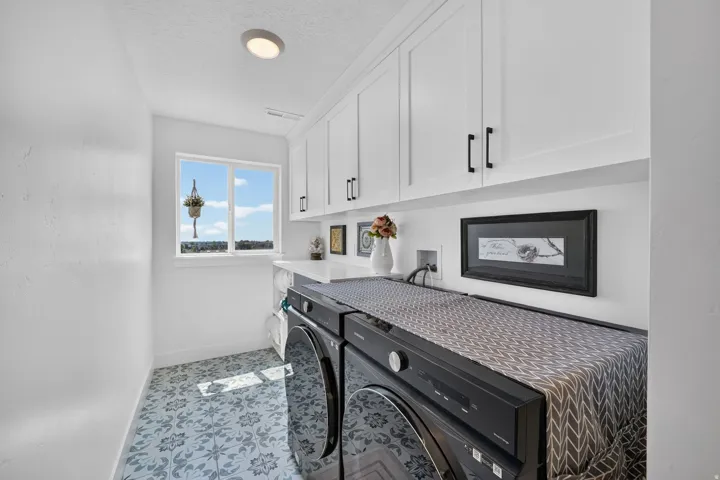 Laundry area featuring white cabinetry with black hardware, a countertop, and patterned floor tiling