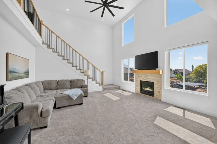 Soaring two-story great room with floor-to-ceiling windows, abundant natural light, and a black modern ceiling fan