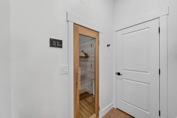 Sauna with a glass-paneled wood door, wood-finish flooring, and white interior walls