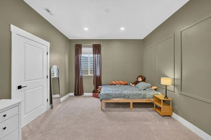 Recessed lighting, panel molding accent wall, window with horizontal blinds, neutral tone carpeting, and a white flat-panel door with black hardware
