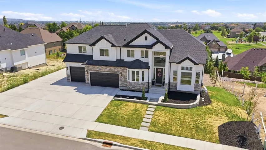 Two-story residence featuring a stone and siding exterior, a large concrete driveway, two dark-toned garage doors, and a well-defined entryway with a prominent front door
