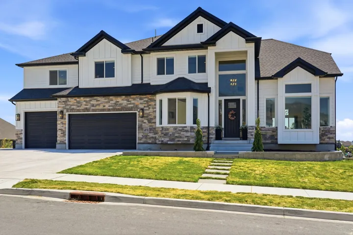 Two-story architectural design, stone and siding exterior, multi-panel garage doors, large front windows, and a concrete driveway