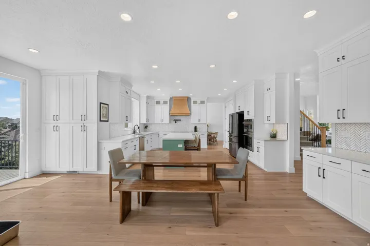 White shaker cabinetry with dark hardware, wood-finish flooring, recessed lighting, and a herringbone tile backsplash