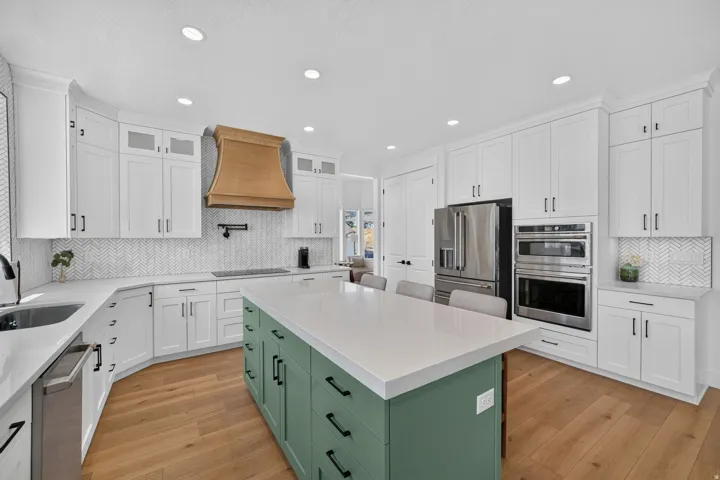 White cabinetry with dark hardware, a wood-finish floor, a green kitchen island with integrated storage, stainless steel appliances, and a tiled backsplash