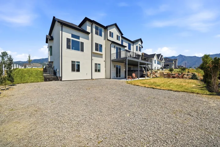 Multi-level stucco exterior with black trim, a second-story deck, a ground-level patio, and a tiered backyard with natural rock landscaping