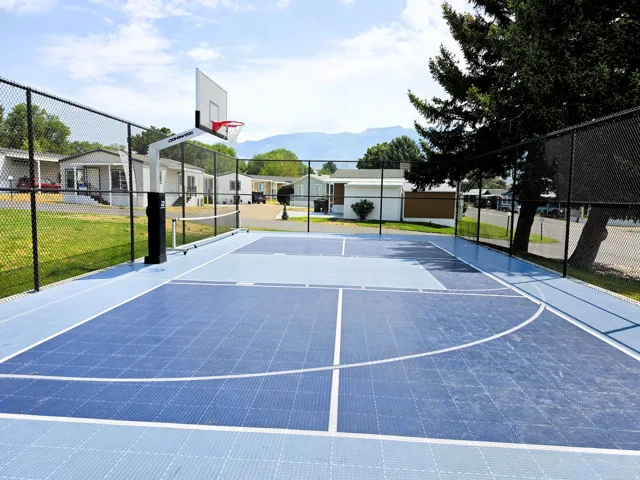 Community outdoor sport court with a basketball hoop, chain-link fencing, and defined court lines