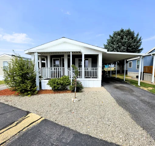 Front porch with white railings, dark siding exterior, gravel landscaping, paved driveway, and covered carport