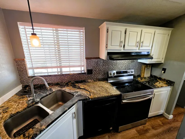 Double basin stainless steel sink, mosaic tile backsplash, granite countertops, white cabinetry, and a stainless steel and black range
