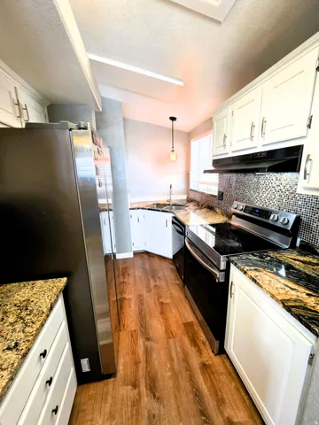 Wood-finish flooring with white cabinetry, granite countertops, and stainless steel appliances