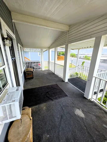 Oversized Covered porch with white railings, and outdoor carpeted flooring.