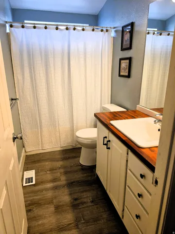 Wood-finish flooring with a white vanity featuring black hardware and a butcher block wood countertop.