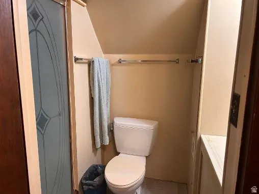 Compact bathroom featuring a white toilet, chrome towel bars, and a shower enclosure with decorative frosted glass