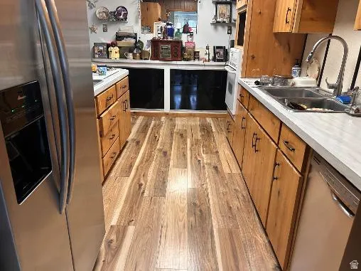 Wood-finish flooring, wood cabinetry with dark hardware, stainless steel refrigerator, stainless steel double basin sink, and white countertops