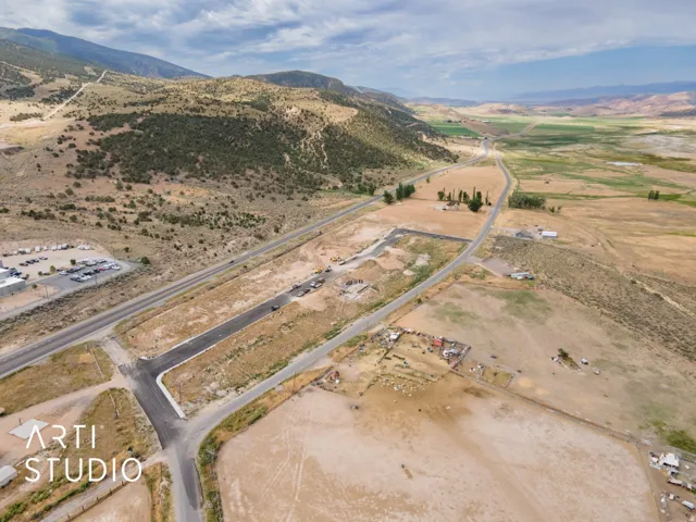 Expansive undeveloped land featuring a paved road, mountainous terrain, and distant green fields