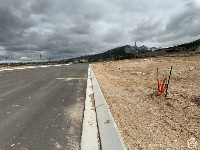 Newly paved asphalt street with a concrete curb, surrounded by undeveloped land and distant mountains
