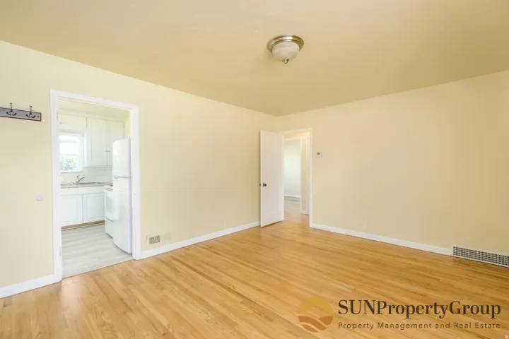 Hardwood flooring, neutral wall color, overhead lighting fixture, white interior doors, kitchen with white cabinetry and appliances