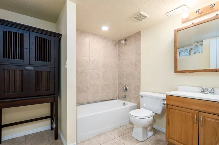 Bathroom featuring a tub/shower combination with tile surround, a single-sink vanity with wood-finish cabinetry, and a mirrored medicine cabinet