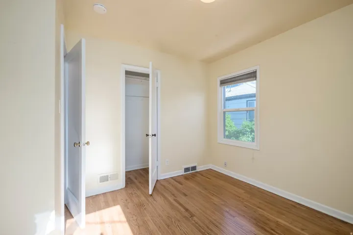 Hardwood flooring, painted walls, white trim, single window with blinds, and a built-in closet