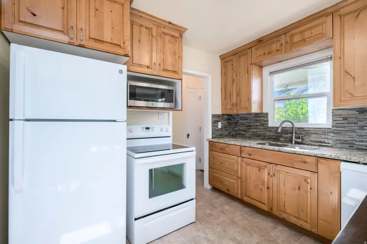 Wood-finish cabinetry paired with a light-toned countertop, mosaic tile backsplash, and a stainless steel sink with a gooseneck faucet