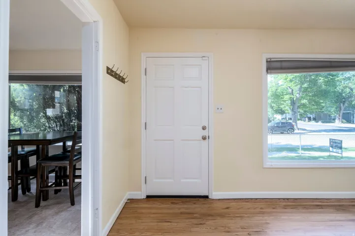 Wood-finish flooring throughout, white paneled door, and a large window providing ambient light