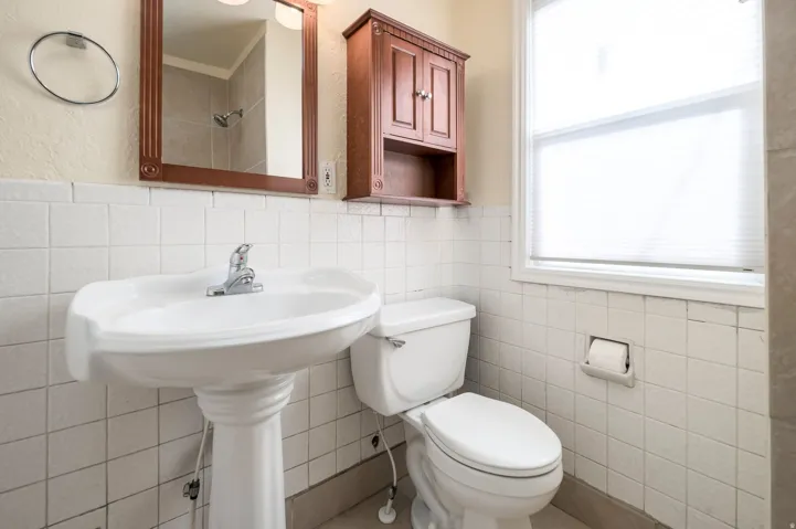 Pedestal sink with chrome faucet, framed mirror, built-in wooden cabinet, and tiled walls