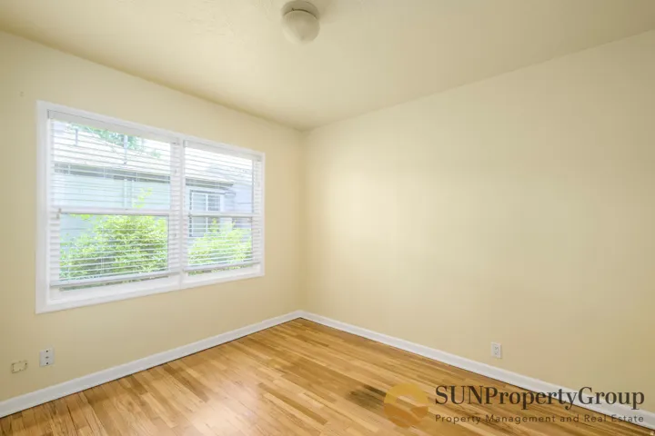 Hardwood flooring with white trim, two large windows, and a ceiling light fixture