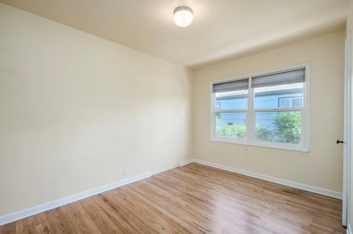 Hardwood flooring, painted walls, ceiling-mounted light fixture, and a white-framed window