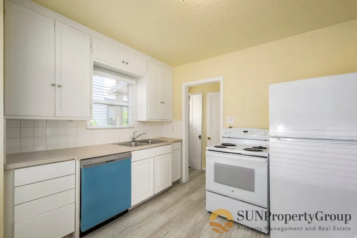 Kitchen featuring white cabinetry, tile backsplash, laminate countertops, a double-basin stainless steel sink, and wood-finish flooring