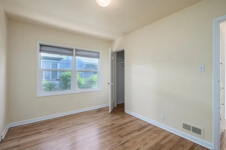 Hardwood flooring, painted walls, two large windows, white trim, and a closet with a built-in shelf